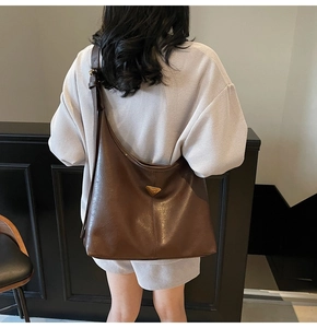 Macro detail of deep brown glossy leather tote featuring triangular metal ornament