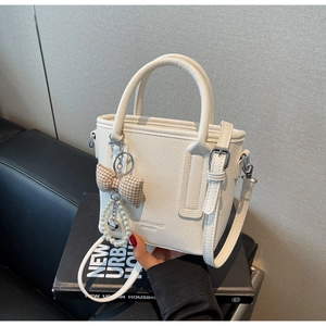 Detail of white lychee leather bucket bag with checkered bow and pearl heart chain strap