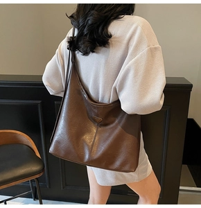 Detail of large dark brown tote bag with metal triangle plaque and leather texture