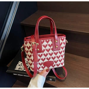 Detail of red heart jacquard pattern on a tote bag with elegant gold hardware and leather trim