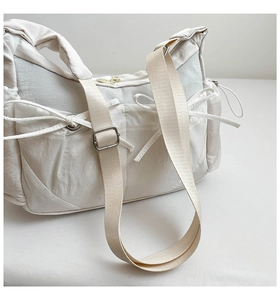 Détail d'un sac à bandoulière en nylon blanc cassé avec poches avant et nœuds décoratifs