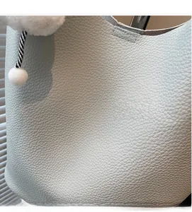 Detail shot of light blue lychee pattern leather bucket bag with soft texture and fur pompom