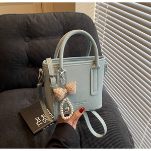 Detail of light blue lychee pattern leather handbag with pearl heart charm and bow