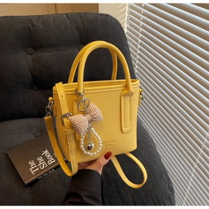 Close-up of bright yellow leather bucket bag with bow pearl charm and lychee texture