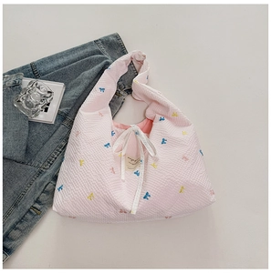 Détail du sac cabas matelassé rose avec broderies de nœuds colorés et ruban blanc