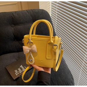 Detail of yellow lychee grain leather handbag with pearl and bow charm accessories