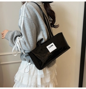 Detailed view of black patent leather shoulder bag with a white minimalist leather brand tag