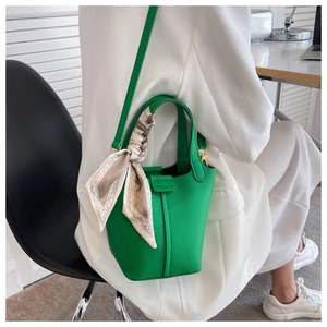 Green leather bucket bag with silk scarf handle detail worn by a model in white