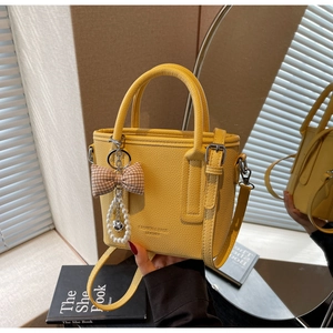 Detail of yellow pebbled leather bucket bag with bow and pearl heart charm accessory