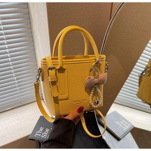 Detail of yellow bucket bag with bow pendant and lychee texture in natural light