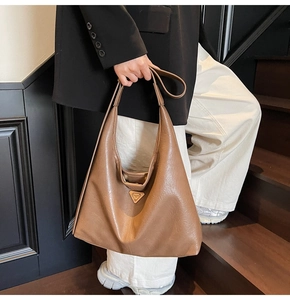 Detail of caramel leather hobo bag with gold triangle plate worn as a shoulder bag