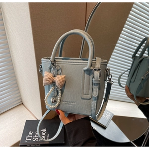 Close-up of light blue pebble leather handbag with elegant bow and pearl charm