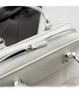 Close-up of smooth silver metal zipper and faux leather texture on white underarm bag