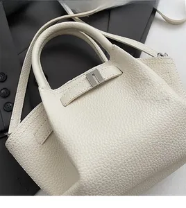 Close-up of beige lychee leather bucket bag with silver buckle and curved top handle