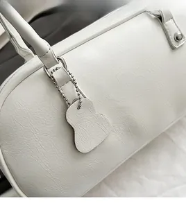 Detail of white baguette bag handle with wrinkled leather texture and bear charm