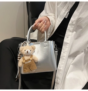 Detail of silver oil-wax leather bucket bag with a cute teddy bear plush charm