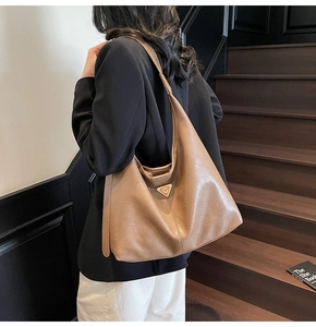 Detail view of a large brown leather hobo bag with a gold triangular metal logo