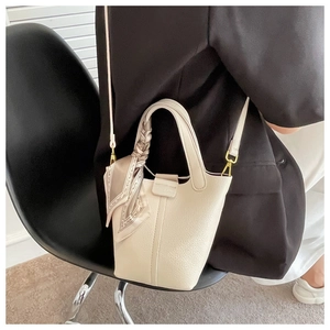 Close-up of beige lychee leather bucket bag with silk scarf and gold hardware detail