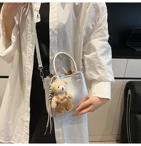 Detail of silver metallic bucket bag with mini handle and plush bear charm accessory