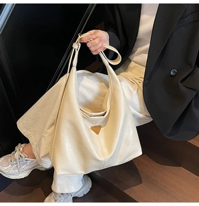 Close-up of cream leather tote bag featuring triangular metal logo and pleated texture