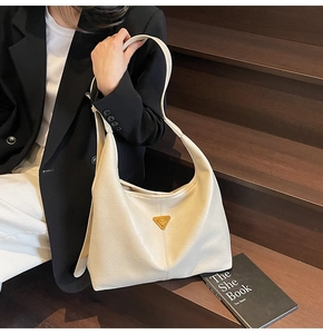 Close-up of cream-colored leather tote bag with gold triangle logo and smooth stitching