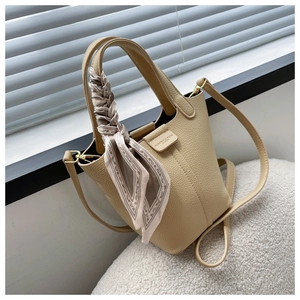 Detail of beige litchi grain bucket bag with decorative silk scarf on the handle
