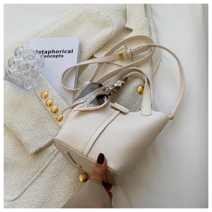 Detail of cream lychee leather bucket bag with decorative silk scarf and gold hardware