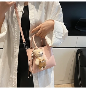 Pink oily leather bucket bag shown as crossbody with cute bear charm and metal buckle
