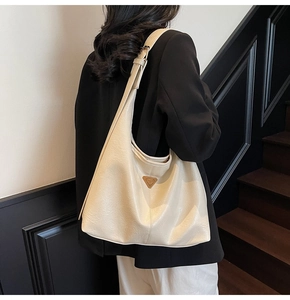 Cream white pebbled leather hobo bag with gold metal logo worn by a model in black blazer