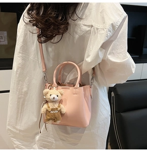 Pink bucket bag with brown bear charm shown as a stylish crossbody on a white shirt
