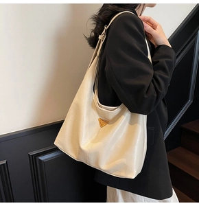 Detail of cream tote bag with triangular metal logo and refined faux leather texture