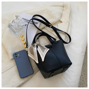 Detail of black pebbled leather bucket bag with gold hardware and elegant floral silk scarf