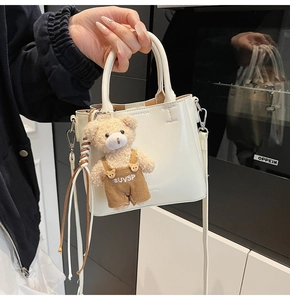 Detail view of cream leather bucket bag with a plush bear charm and adjustable shoulder strap