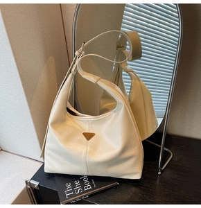 Macro shot of cream hobo tote featuring soft leather texture and golden metal logo plaque