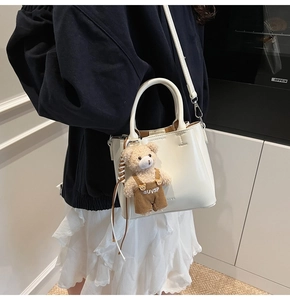 Detailed side view of white faux leather bucket bag with a cute plush bear charm