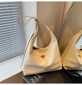 Detail of a beige tote bag featuring litchi texture leather and triangle metal plaque