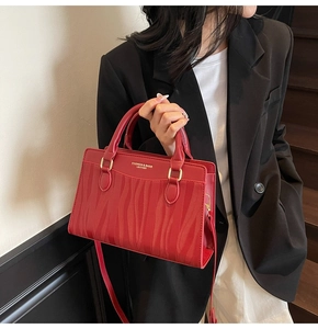 Detailed close-up of red leather tote bag with wavy texture and gold embossed fashion logo