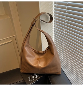 Detailed view of brown leather crescent bag with adjustable strap and golden logo