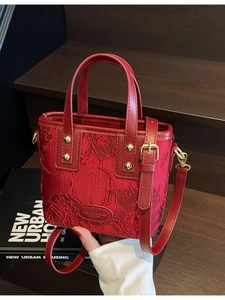 Elegant red bridal handbag with floral texture and leather handles on wooden steps