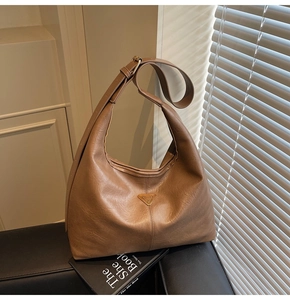 Close-up detail of the brown pebbled leather texture and triangular metal logo on the hobo bag