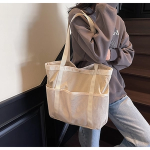 Detalle de un bolso tipo cubo de lona beige con bolsillos de malla blanca en el frente