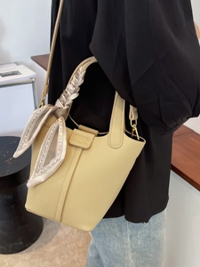 Chic beige leather bucket bag with silk scarf handle detail and gold hardware on model