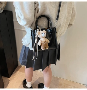 Detail of black oil-wax texture bucket bag with cute bear charm and shoulder strap