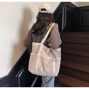 Detalle de un bolso tote grande beige con bolsillos de malla blanca y correa ancha al hombro