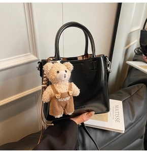 Detail of a black patent leather bucket bag with a cute beige teddy bear charm accessory