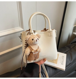 Detail of cream bucket bag with textured leather and cute teddy bear charm accessory