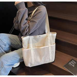 Detalle de bolsa tote de lona beige con bolsillo de malla blanca y cierre de presión