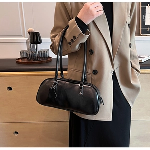 Detail of a minimalist black bowling-style underarm bag with glossy texture and slim straps