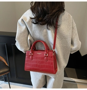 Detail of red crocodile texture handbag with gold hardware held by a woman in a red dress