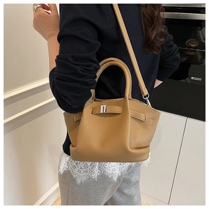 Brown lychee leather bucket bag with silver buckle worn by a model in a modern kitchen